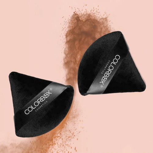 Two black makeup sponges with 'ColorBox' branding on a pink background with brown powder.